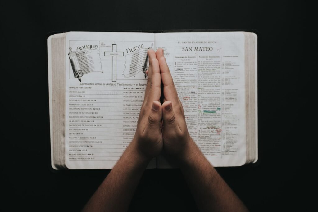 Hands folded in prayer over an open Bible (photo: Pexels)